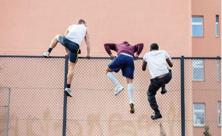 Drei junge Männer klettern über einen Zaun – Beispiel für ungewöhnliche Bildsprache in der Bildredaktion